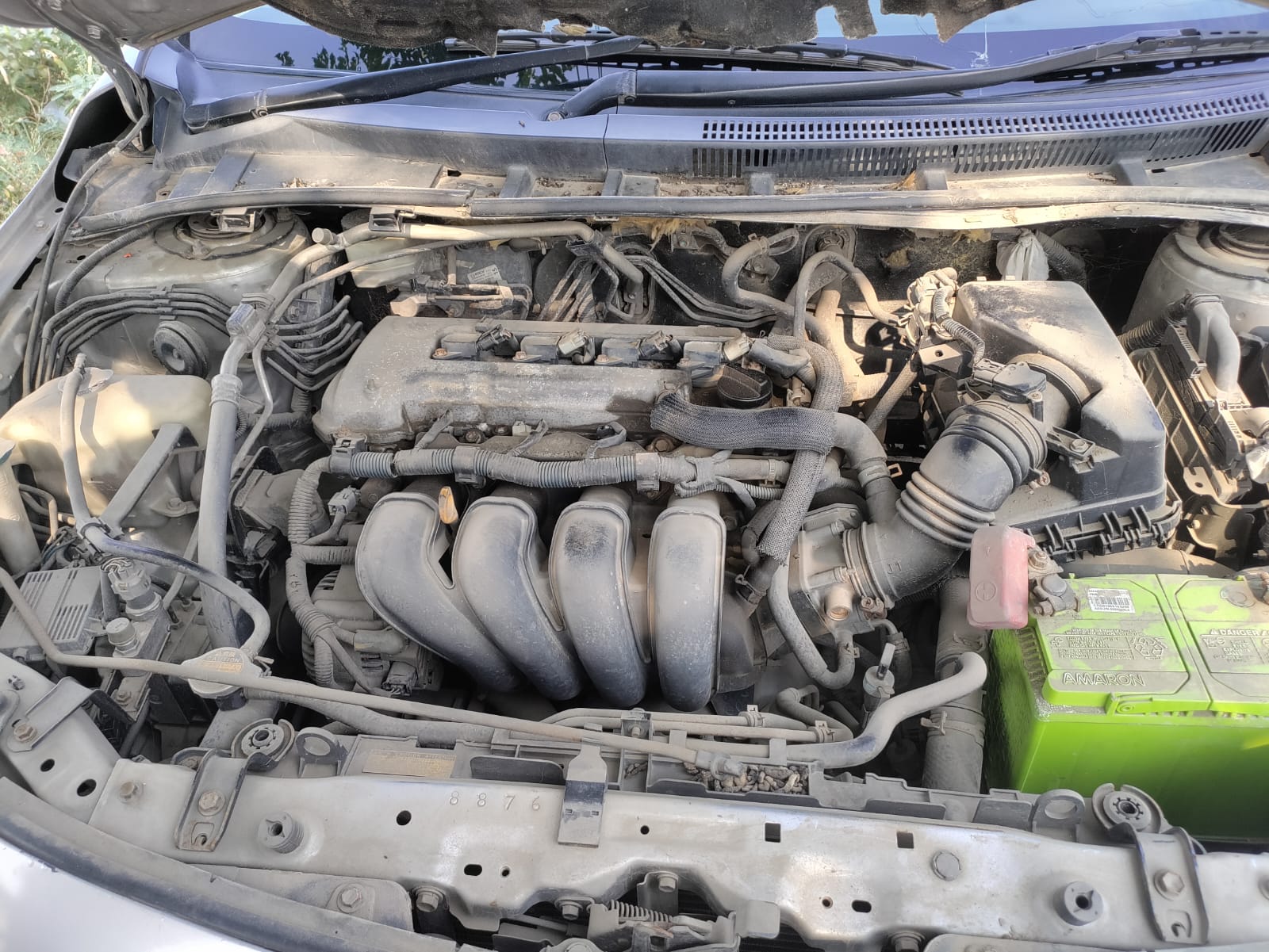 Petrol engine bay view with battery, intake, wiring, and manifold