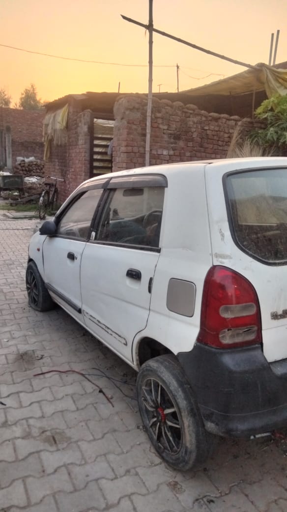 Old white Maruti Alto side and rear view parked near brick structure