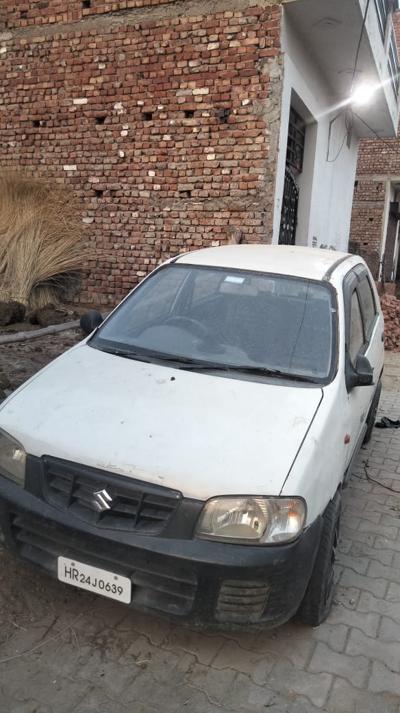 Old white Maruti Alto front view parked beside brick wall